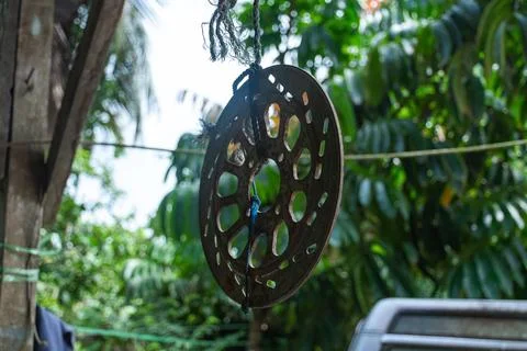 Large circular perforated metal object hanging by rope outdoors with green .. Stock Photos