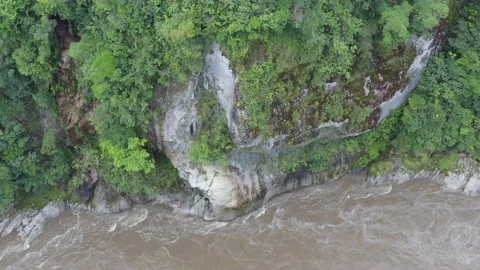 A large cliff overgrown with small plants next to a dangerous river Stock Footage 143676398