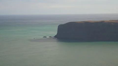 Large cliffs jutting out into the blue ocean on a clear day, in New Zealand Stock Footage 217395874