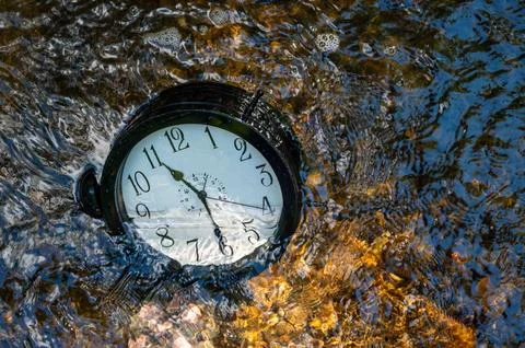 A large clock half submerged in a flowing stream with ripples pebbles Stock Photos