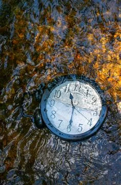 A large clock half submerged in a flowing stream with pebbles vertical Foto stock
