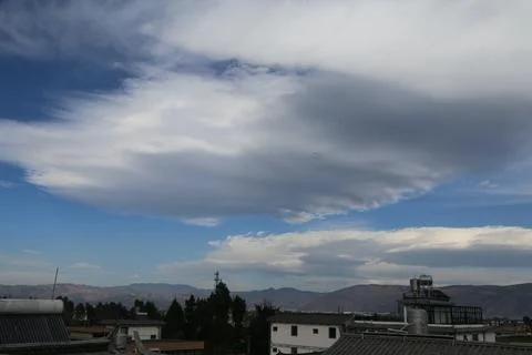 Large cloud formation above rooftops and distant mountains Фото