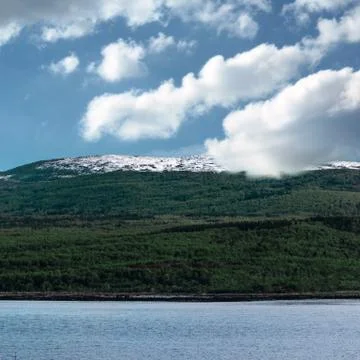 A large cloud sets on the green mountain hill with snow on top. Murmansk Russ Stock Photos