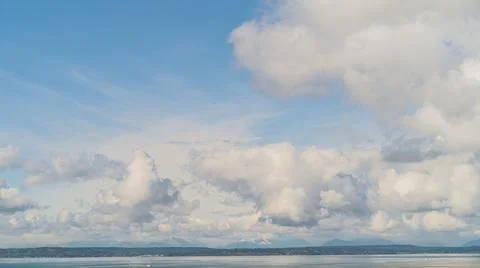 Large clouds and blue sky obscure Olympic Mountain Range in Pacific Northwest Stock Photos
