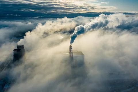 Large clouds of white smoke cover power plant territory under bright sunlight on Stock Photos