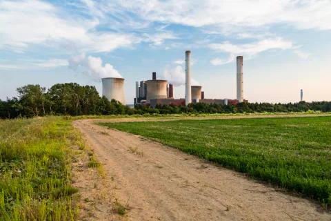 A large coal-fired power station behind a hill with a dirt road leading towar Stock Photos