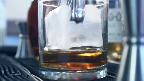 Large cocktail ice cube placed in whiskey on bar ma  Stock Footage 87266934