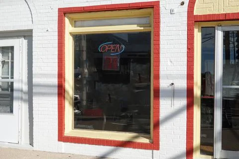 Large colorful store front window with a neon open sign and a red painted bor Stock Photos