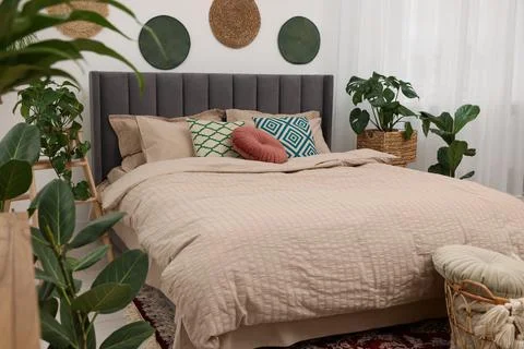 Large comfortable bed and potted houseplants in stylish bedroom. Interior d.. 스톡 사진