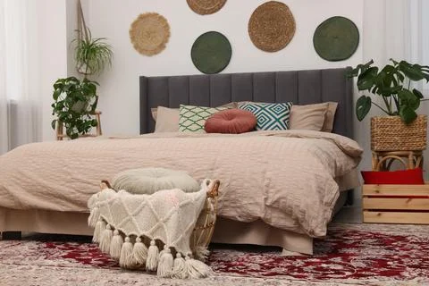 Large comfortable bed and potted houseplants in stylish bedroom. Interior d.. 스톡 사진