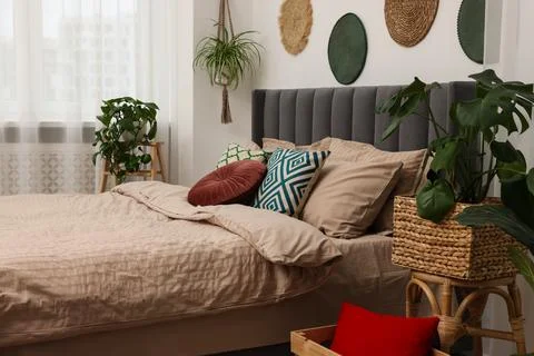 Large comfortable bed and potted houseplants in stylish bedroom. Interior d.. 스톡 사진