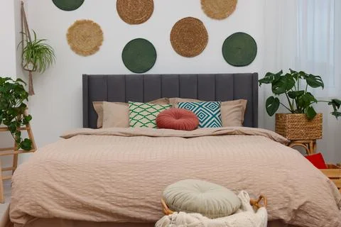 Large comfortable bed and potted houseplants in stylish bedroom. Interior d.. 스톡 사진