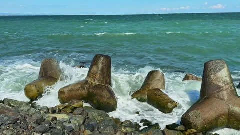 Large concrete blocks on a rocky shore with waves crashing against them in the Stock Footage 340149703