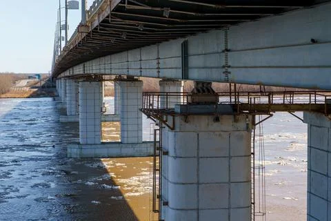 Large concrete bridge pillars over muddy river with floating ice. Stock Photos