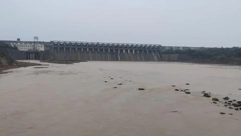 Large concrete dam spanning a wide muddy river during monsoon, with multiple spi Stock Photos