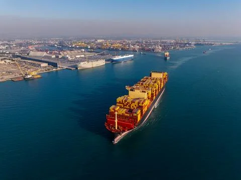 Large Container Cargo Ship Navigating Near Industrial Seaport Terminal In L.. Fotos de archivo