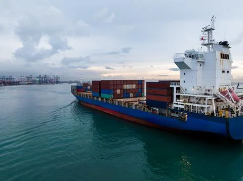 Large Container Cargo Ship Sailing Through Busy International Harbor At Dusk Stock Photos