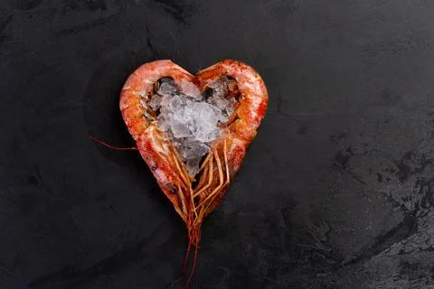 Large cooked shrimp lie in the shape of a heart on a dark background. Stock Photos