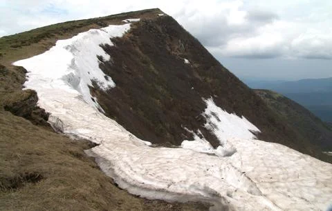 Large cornice of snow clinging to a steep mountain peak ridge in spring Stock Photos