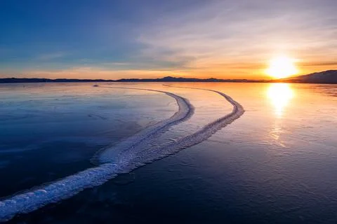 Large cracks in the clear smooth blue ice of Lake Baikal at sunset. Siberia Stock Photos