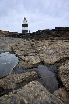Large cracks in rocks with Hook lighthouse at the bottom. Wexford, Ireland. Stock Photos