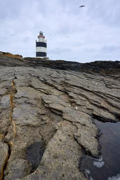 Large cracks in rocks with Hook lighthouse at the bottom. Wexford, Ireland. Stock Photos