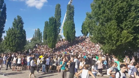 Large crowd around Bearpit karaoke, Mauerpark, people walk, trees, sunny, Berlin 스톡 동영상 77410111
