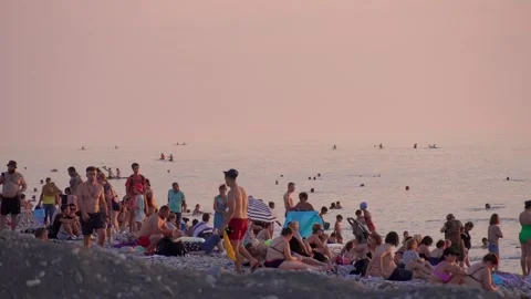 Large crowd standing on beach watching sunset over ocean. Видео 250561029