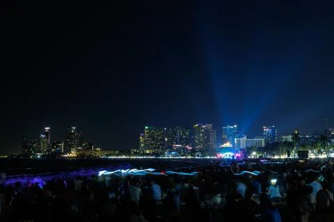 Large Crowd Watching Light Show On Sandy Beach With Glowing City Skyline At.. Foto stock