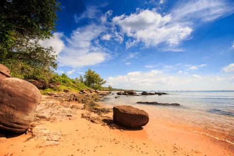 Large cube stone on sand beach by transparent water under low tide against gr Stock-Fotos