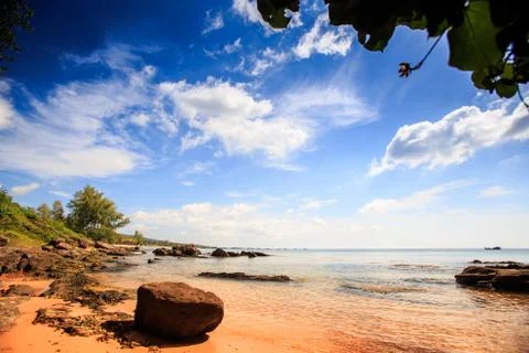 Large cube stone on sand beach by transparent water under low tide against gr 写真素材