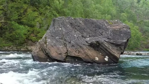 A large, dark boulder sits half-submerged in a rushing river. Stock Footage 321997292