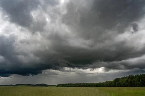 Large dark clouds dominate the sky above a rural meadow and forest landscape Stock Photos
