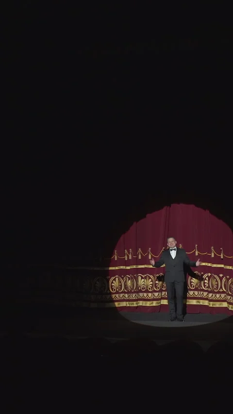 A large dark hall with a stage lit by a round soffit. A red curtain from behind Vídeo Stock 275024646