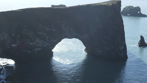 A large, dark rock formation forming a natural arch in the sea. Stock Footage 335963747