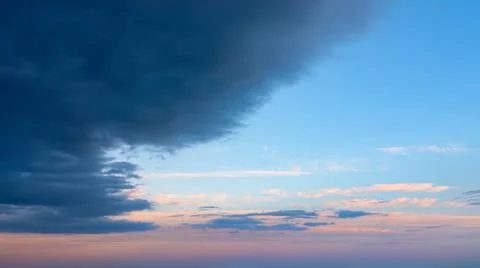 Large dark storm cloud obscures the clear pink blue vanilla sky at dawn. Stock Photos