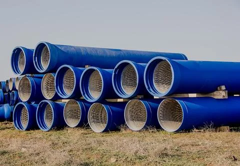 Large diameter blue concrete pipes lie in the field. Stock Photos
