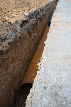 Large diameter water pipe in earthen trench under asphalt street surface Stock Photos
