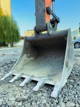 A large digging bucket of a machine sits on gravel in a city area. The sun is Fotos de archivo