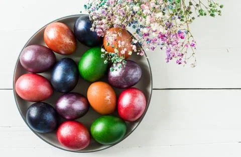 A large dish with colorful Easter eggs and flowers on a white wooden backgr.. Stock Photos