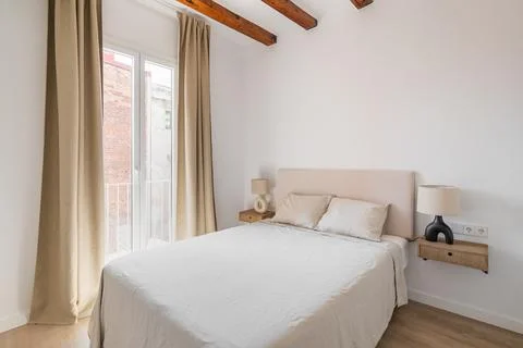 Large double bed with light linens. Spacious light bedroom with a large window Photos