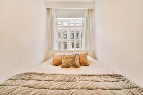 A large double bed right next to a large bright window Stock Photos