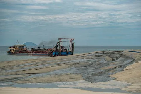 Large Dredging Ship Pumping Dark Slurry Onto a Sandy Beach Foto stock