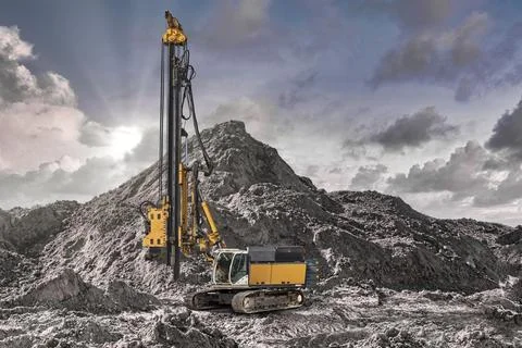 A large drilling machine works on a construction site, surrounded by mounds o Stock Photos