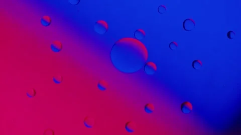 A large drop absorbs several smaller drops on a blue-red gradient background. 動画素材 303058702
