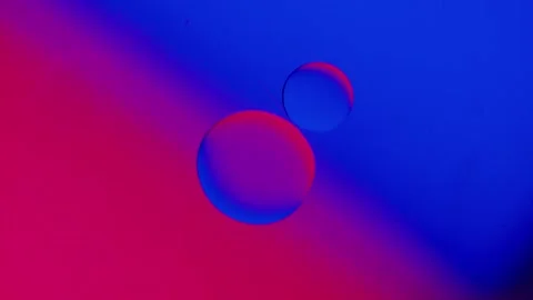 A large drop absorbs a smaller drop on a blue-red gradient background. Vídeo Stock 303058599