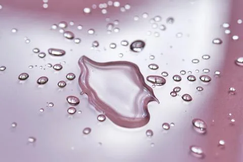 A large drop and splashes of micellar water on a pink background. Stock Photos