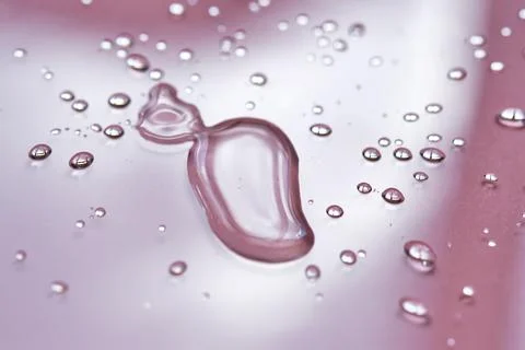 A large drop and splashes of micellar water on a pink background. Stock Photos