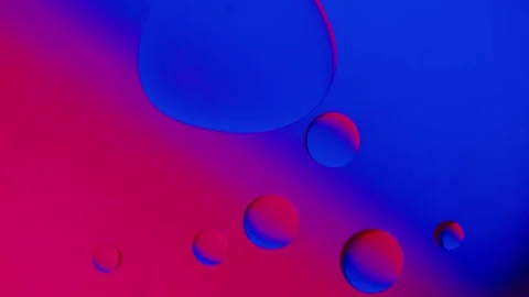 A large drop of oil absorbs small drops on a blue-red gradient background. 스톡 동영상 303058595