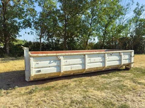 Large dumpster placed on a grassy field by some trees during the day Stock Photos